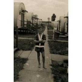 Ronald Pearson standing on a path between Nissen huts, Cabramatta Migrant Hostel, Cabramatta NSW